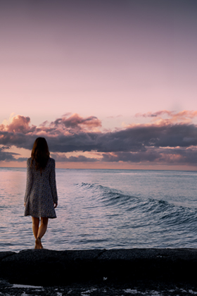 Woman standing at the edge of the ocean at dusk.